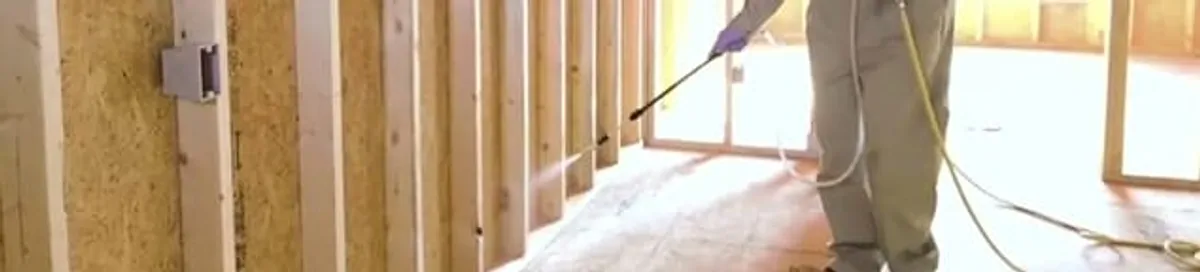 Termite treatment technician applying spray along framing and unfinished walls in Myrtle Beach, SC